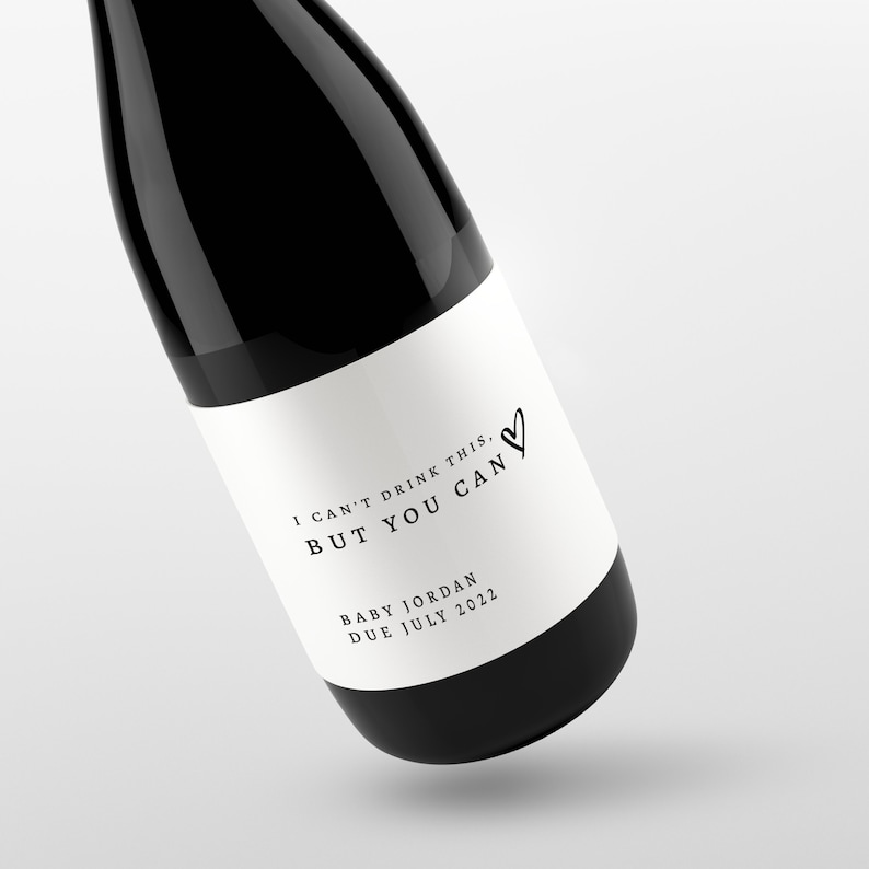 May include: A black wine bottle with a white label. The label reads "I CAN'T DRINK THIS. BUT YOU CAN" with a heart symbol. Below the text is "BABY JORDAN DUE JULY 2022".