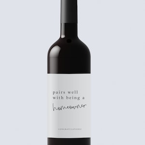 May include: A dark wine bottle with a black top and a white label. The label reads "pairs well with being a homeowner" and "CONGRATULATIONS!". The bottle is filled with red wine.