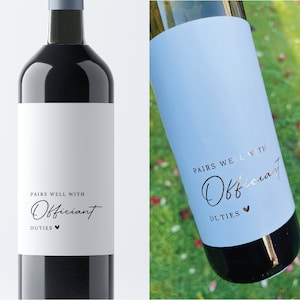 May include: Two wine bottles with labels that say "Pairs well with Officiant Duties" in black script. One bottle has a white label and the other has a light blue label.