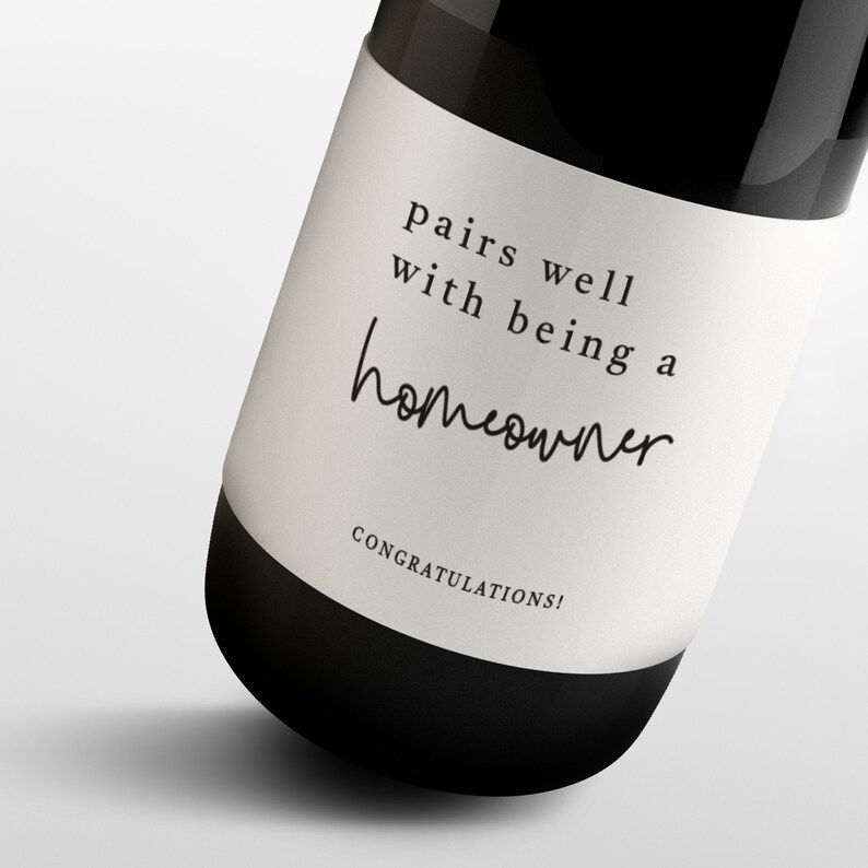 May include: A black wine bottle with a white label. The label reads "pairs well with being a homeowner" in a mix of serif and script fonts. "Congratulations!" is printed at the bottom of the label.