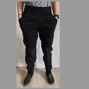 May include: Black high-waisted pants with a wide waistband and pockets. The pants have a relaxed fit through the hips and thighs, tapering to the ankles. The model is wearing black shoes.