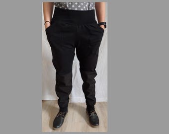 Puede incluir: Pantalones negros de cintura alta con una cinturilla ancha y bolsillos. Los pantalones tienen un corte holgado en las caderas y muslos, estrechándose hacia los tobillos. El modelo lleva zapatos negros.