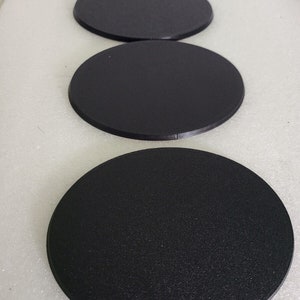 May include: Three black round plastic bases for miniature figures. The bases are smooth and have a slightly textured surface.