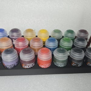 May include: A black paint rack with 18 small paint bottles. The bottles are arranged in three rows of six. The bottles are labeled "Citadel Colour".