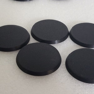 May include: Six black round plastic bases for miniature figures. The bases are smooth and have a slightly raised edge.
