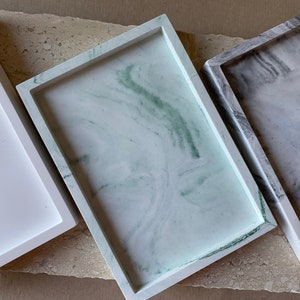 Könnte beinhalten: Drei rechteckige Tabletts aus weißem Marmor mit unterschiedlichen Mustern. Die Tabletts sind in einer Reihe angeordnet, mit dem weißen Tablett links, dem grünen Marmortablett in der Mitte und dem grauen Marmortablett rechts.