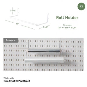 Puede incluir: Porta rollo de metal blanco para un tablero de clavijas. El porta rollo mide 25,4 cm de largo, 10,5 cm de alto y 5,4 cm de profundidad. Se muestra sosteniendo un rollo de film transparente y un rollo de papel de aluminio. El texto "Roll Holder" y "Dimension: 10" * 4-1/8" * 2-1/8"" es visible en la imagen. El texto "Works with Ikea SKÅDIS Peg Board" también es visible en la imagen.