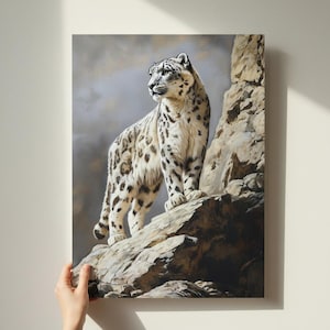 May include: A canvas print depicting a snow leopard on a rocky outcrop. The big cat has white fur with black spots and is looking left. The background is a cloudy, muted grey.