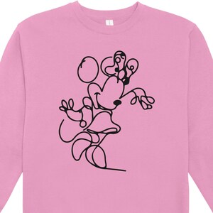 May include: Pink sweatshirt featuring a black line drawing of a cartoon character. The design depicts a character with large ears, a bow, and a skirt. The sweatshirt has a crew neck and long sleeves, suitable for casual wear.
