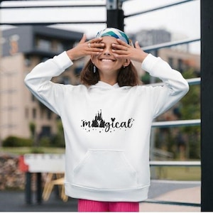 Op de afbeelding: Witte hoodie met een zwarte afbeelding van een kasteel en het woord "magical" op de voorkant.