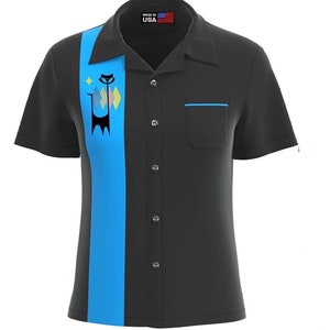 May include: A black short-sleeved button-up shirt with a blue stripe down the center. The stripe features a black cat design with a yellow star and pink and blue diamonds. The shirt has a blue pocket on the left side and says "Made in USA" on the collar.