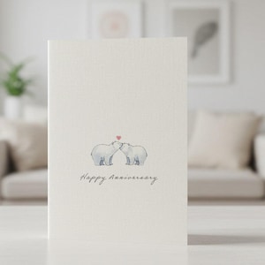 May include: A white card with a drawing of two polar bears kissing with a red heart above them. The text "Happy Anniversary" is written below the bears.