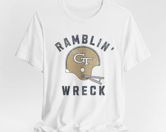 May include: White t-shirt with a vintage-style graphic of a gold football helmet with the letters "GT" on it. The text "Ramblin' Wreck" is printed below the helmet.