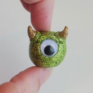 Könnte beinhalten: Grüner Glitzermonster mit einem einzigen Glitzera Auge und goldenen Glitzerhörnern.