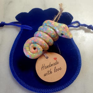 May include: A handmade, colorful, glittery, coiled snake charm, with a tag that reads "Handmade with love".