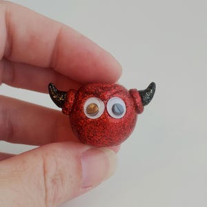 May include: A small red glitter devil ornament with black horns and googly eyes.