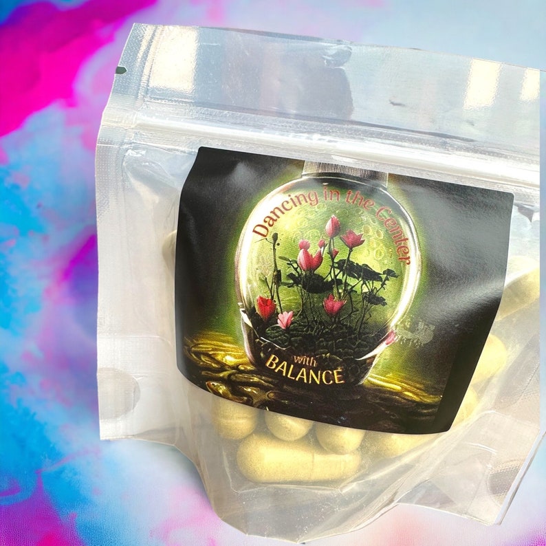 May include: A clear plastic bag filled with light green capsules. The bag has a label with a graphic of a glass orb containing pink lotus flowers and the text "Dancing in the Center with BALANCE".