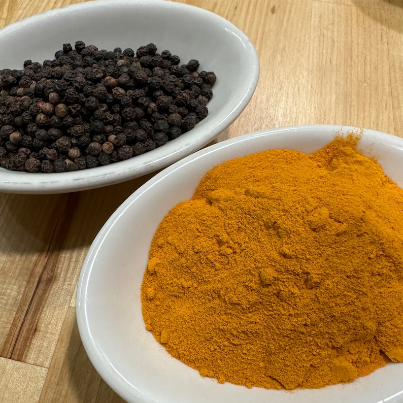 May include: Two white bowls, one filled with black peppercorns and the other with a mound of bright yellow turmeric powder.