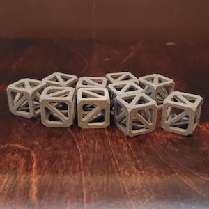 Op de afbeelding: Een groep van tien grijze, 3D-geprinte, geometrische dobbelstenen met een hol, open ontwerp.