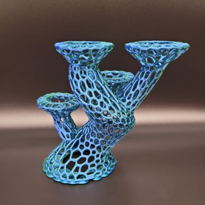 Può includere: Un oggetto decorativo stampato in 3D blu e verde con un design unico, organico e ramificato. L'oggetto ha tre cime aperte e una base che ricorda un tronco d'albero.