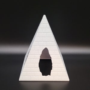 May include: A white pyramid-shaped decorative object with a rectangular opening. The pyramid has a textured, brick-like surface. The background is a solid black.
