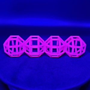 May include: Four pink geometric shapes, resembling open cages, are lined up in a row on a dark blue surface. The shapes are made of a translucent material and appear to be glowing under a black light.
