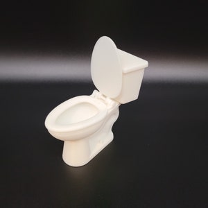 Op de afbeelding: Een wit keramiek toilet met de deksel omhoog. Het toilet is een miniatuurversie van een standaard toilet.