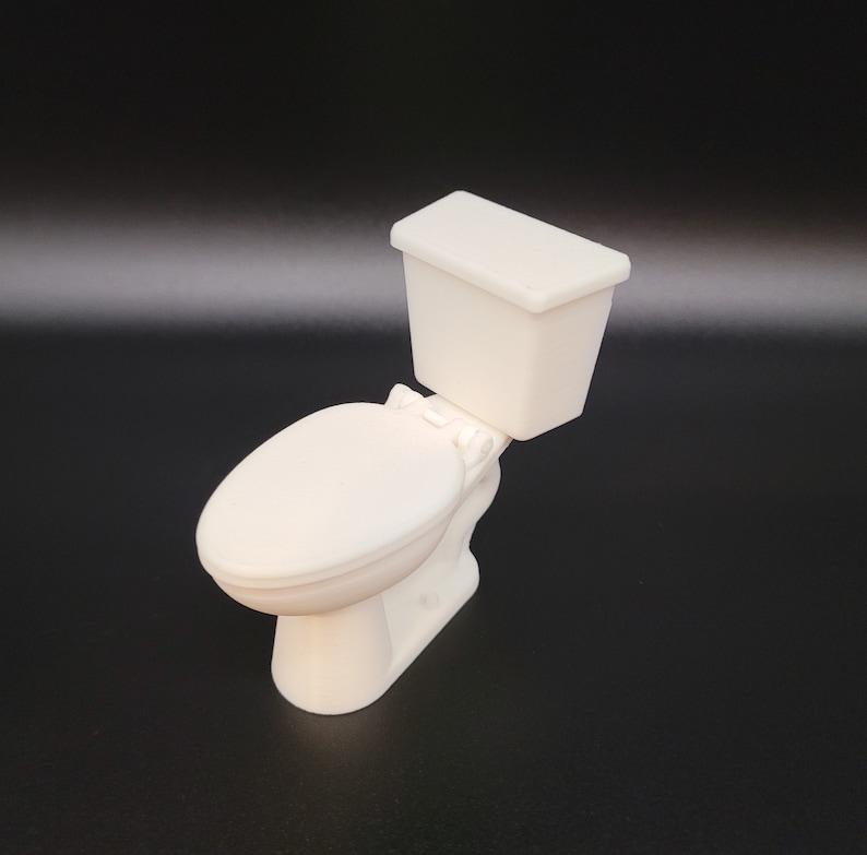 Op de afbeelding: Een wit plastic miniatuurtoilet met een gesloten deksel. Het toilet is een klein model van een echt toilet.