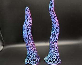 May include: Two abstract sculptures with a lattice design. The sculptures are tall and curved, with a gradient of colors from purple to blue to teal. The bases are flared, and the overall effect is organic and modern.
