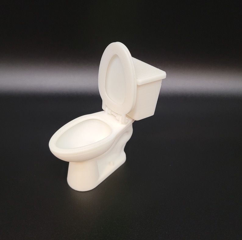 Op de afbeelding: Een wit plastic miniatuurtoilet met een gesloten deksel en een aparte tank. Het toilet is een klein model van een echt toilet.