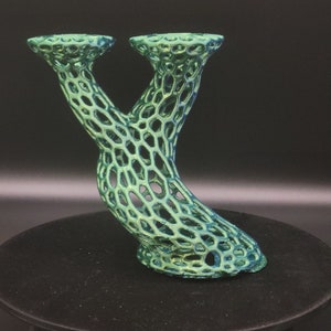 May include: A green and blue 3D printed vase with a lattice design. The vase has two openings at the top and a curved base.