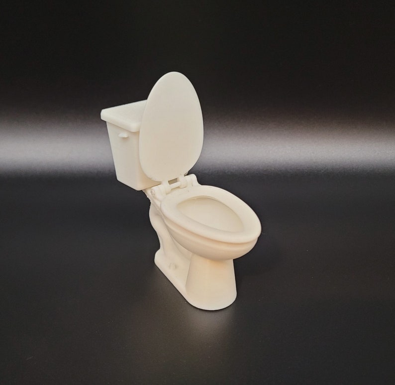 Op de afbeelding: Een wit plastic model van een toilet met de deksel omhoog.