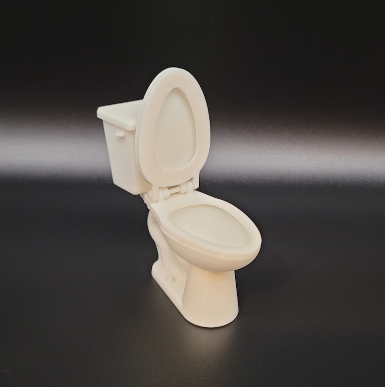 Op de afbeelding: Een wit keramiek toilet met de deksel open. Het toilet is een miniatuurversie van een standaard toilet.