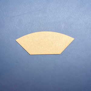 以下が含まれることがあります： 平らな底と湾曲した上部を持つ、薄茶色の扇形のオブジェクト。オブジェクトは明るい色の素材でできており、濃い青色の背景に配置されています。形状はコーヒーフィルターに似ています。