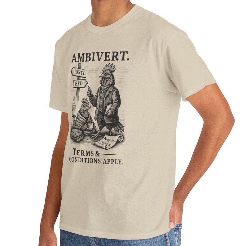 May include: Beige t-shirt with a black and white illustration of two anthropomorphic chickens. One chicken is wearing a suit and holding a scroll. The shirt reads "AMBIVERT." with directional signs pointing to "PARTY" and "BED."