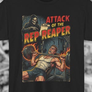 May include: Black t-shirt featuring a comic book style illustration. The graphic depicts a weightlifter struggling with a barbell, with a Grim Reaper figure looming above. Text reads "ATTACK OF THE REP REAPER".