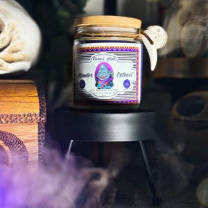 Pode incluir: Um frasco de vela roxo e dourado com uma tampa de madeira. O r&oacute;tulo diz "Hero's Milk" e "Monster Extract". A vela &eacute; 100% cera de soja natural e feita &agrave; m&atilde;o no Arkansas.