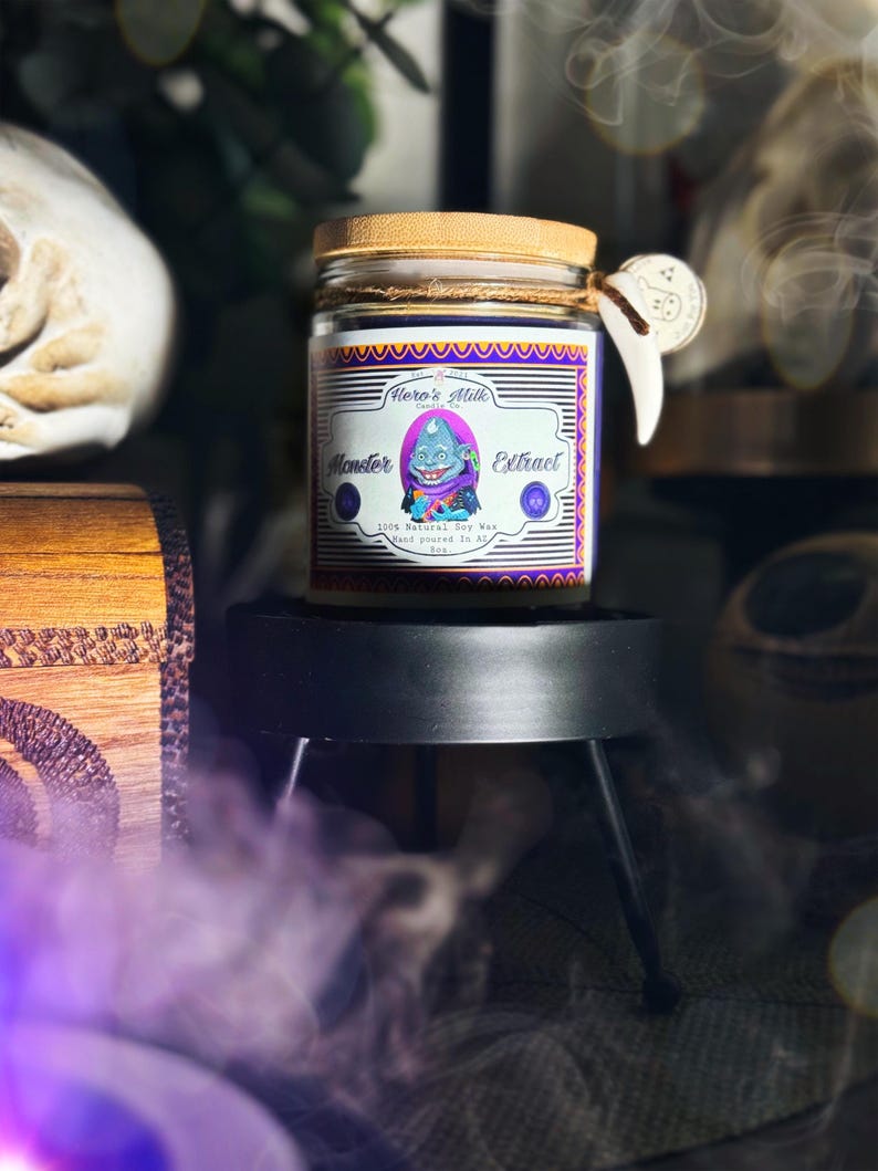Pode incluir: Um frasco de vela roxo e dourado com uma tampa de madeira. O r&oacute;tulo diz "Hero's Milk" e "Monster Extract". A vela &eacute; 100% cera de soja natural e feita &agrave; m&atilde;o no Arkansas.