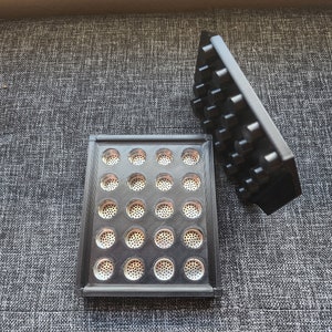 May include: Two black plastic trays with a grid of small, round, silver-colored metal mesh inserts. The trays are on a gray fabric surface.