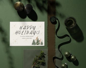 May include: A rectangular greeting card with a cream background featuring the black text HAPPY HOLIDAYS, A LITTLE APPRECIATION GOES A LONG WAY, gold star accents, and a watercolor illustration of deer standing among green pine trees.