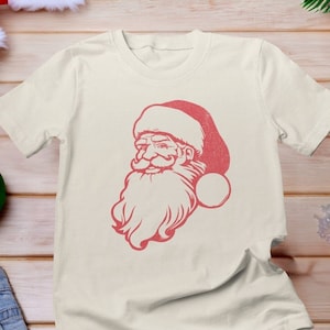May include: A white t-shirt featuring a red vintage-style illustration of Santa Claus's face on the front.