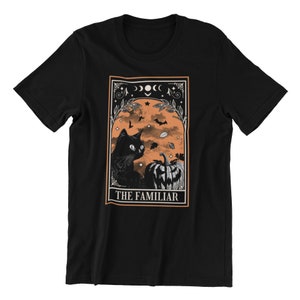 Pu&ograve; includere: T-shirt nero con un design a tema Halloween. La grafica presenta un gatto nero, una zucca intagliata, pipistrelli e la scritta "THE FAMILIAR" in una cornice decorativa. Lo sfondo &egrave; arancione, in stile vintage.
