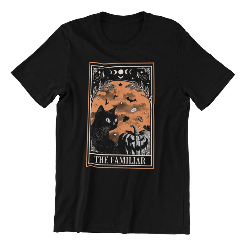 Pu&ograve; includere: T-shirt nero con un design a tema Halloween. La grafica presenta un gatto nero, una zucca intagliata, pipistrelli e la scritta "THE FAMILIAR" in una cornice decorativa. Lo sfondo &egrave; arancione, in stile vintage.