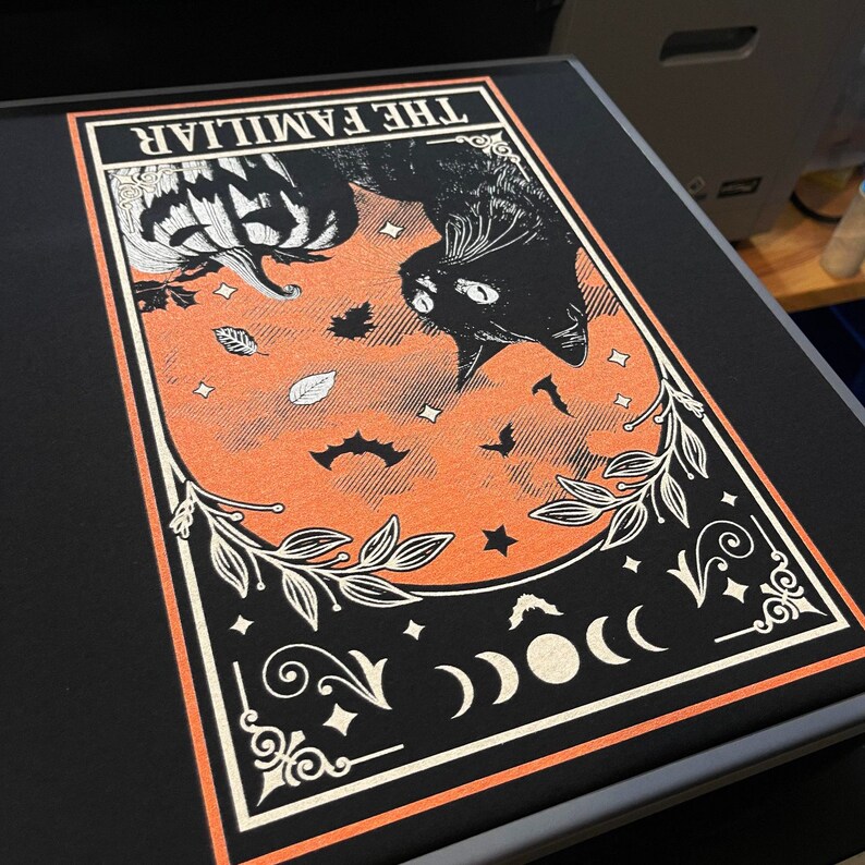 Pu&ograve; includere: Stampa grafica nera con un gatto nero, una zucca, pipistrelli e la scritta "THE FAMILIAR" su sfondo arancione. Il design &egrave; incorniciato da un bordo bianco ed elementi floreali decorativi, ideale per Halloween o decorazioni gotiche.