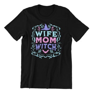 Pu&ograve; includere: Maglietta nera con un design blu e rosa che dice "Wife Mom Witch" con un cappello da strega e teschi.