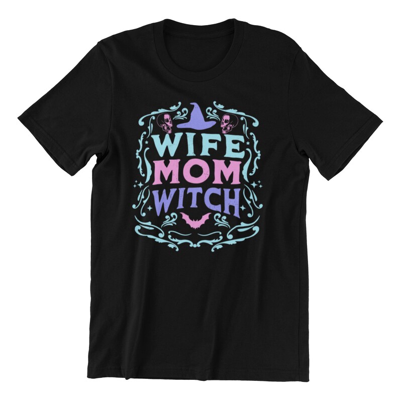 Pu&ograve; includere: Maglietta nera con un design blu e rosa che dice "Wife Mom Witch" con un cappello da strega e teschi.