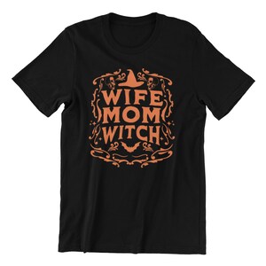 Pu&ograve; includere: Maglietta nera con un design grafico arancione che dice "Wife Mom Witch" con un cappello da strega e teschi.