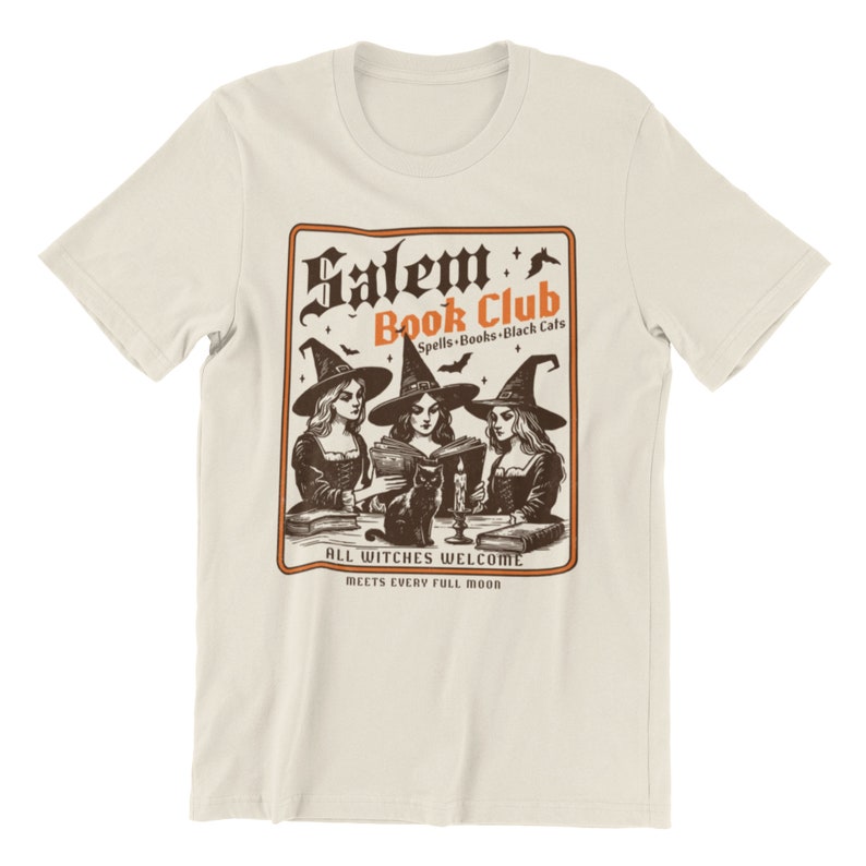 May include: A beige t-shirt with a vintage-style illustration of three witches reading books in a circle. The text reads "Salem Book Club Spells-Books-Black Cats All Witches Welcome Meets Every Full Moon".