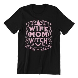 Pu&ograve; includere: Maglietta nera con un design grafico rosa che dice "Wife Mom Witch" con un cappello da strega e pipistrelli.