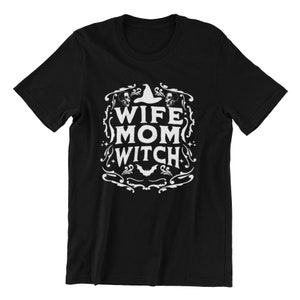 Pu&ograve; includere: Maglietta nera con un design grafico bianco che dice "Wife Mom Witch" con un cappello da strega e teschi.
